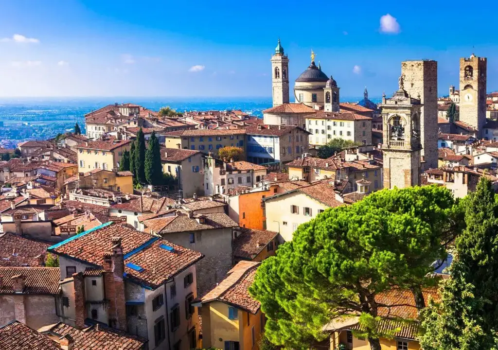 Panorama da cidade alta de Bérgamo, na Lombardia, com torres medievais, telhados de terracota e igrejas históricas em meio ao verde das colinas.