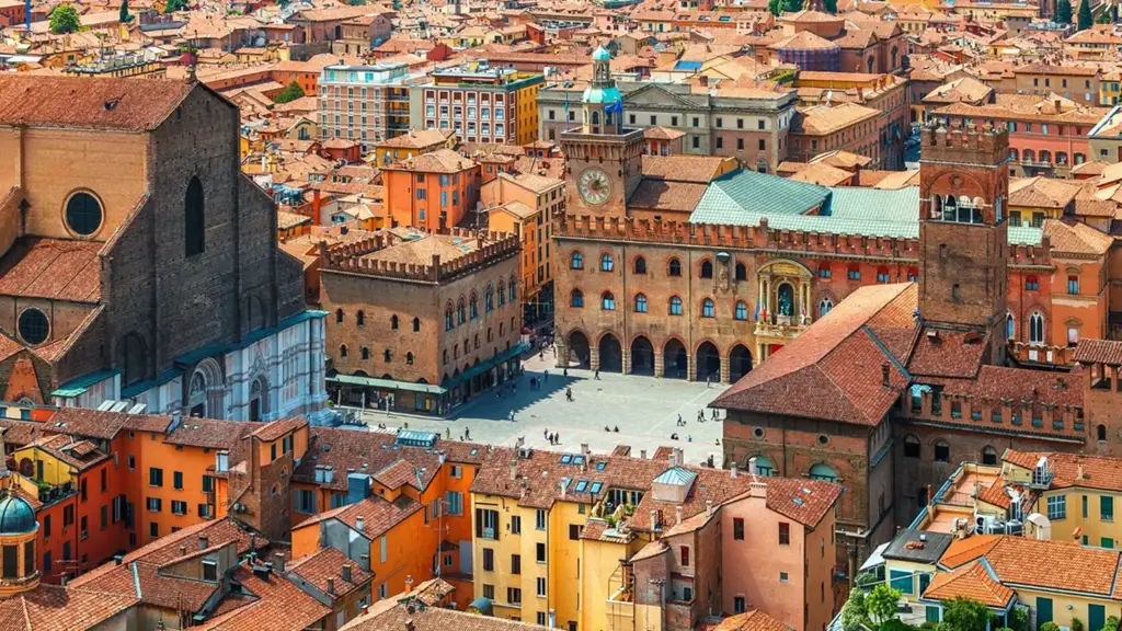 Vista aérea do centro histórico de Bolonha, com destaque para a Piazza Maggiore, a Basílica de San Petronio à esquerda e construções medievais com telhados terracota ao redor.