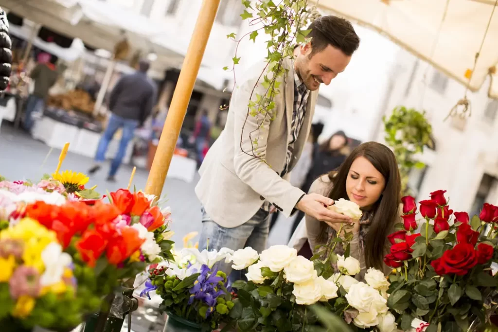Casal sorridente escolhendo flores frescas em uma feira ao ar livre na Toscana durante a primavera