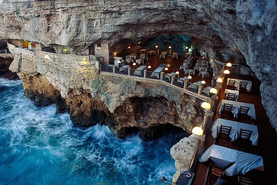 Restaurante Grotta Palazzese em Polignano a Mare, com mesas dispostas dentro de uma caverna sobre o mar Adriático, criando um ambiente único e impressionante

