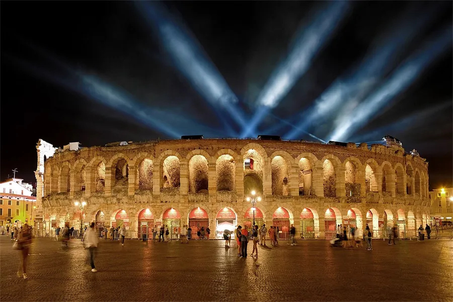 Arena di Verona iluminada à noite com fachos de luz no céu, antes de uma apresentação do festival de ópera, na Itália.