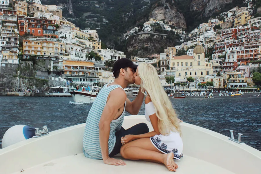Casal se beijando na proa de um barco em frente à vila colorida de Positano, na Costa Amalfitana, durante passeio romântico pelo mar. 