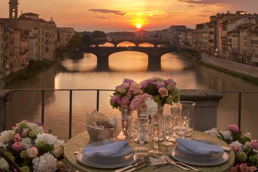 Mesa decorada para jantar romântico ao pôr do sol com vista para a Ponte Vecchio e o Rio Arno, em Florença.