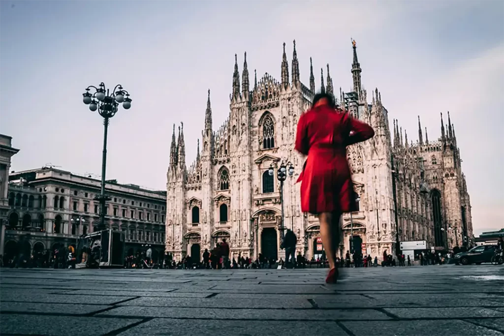 Mulher com vestido vermelho caminhando diante do Duomo de Milão, unindo arquitetura icônica e estilo da Moda Italiana.

