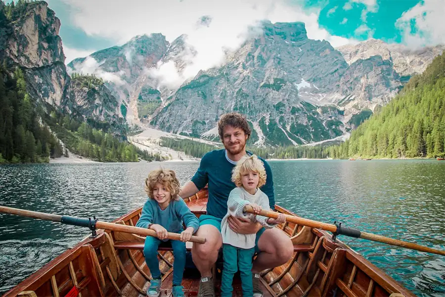 Pai com dois filhos em um passeio de barco no Lago di Braies, cercado pelas montanhas das Dolomitas, durante uma viagem em família para a Itália.