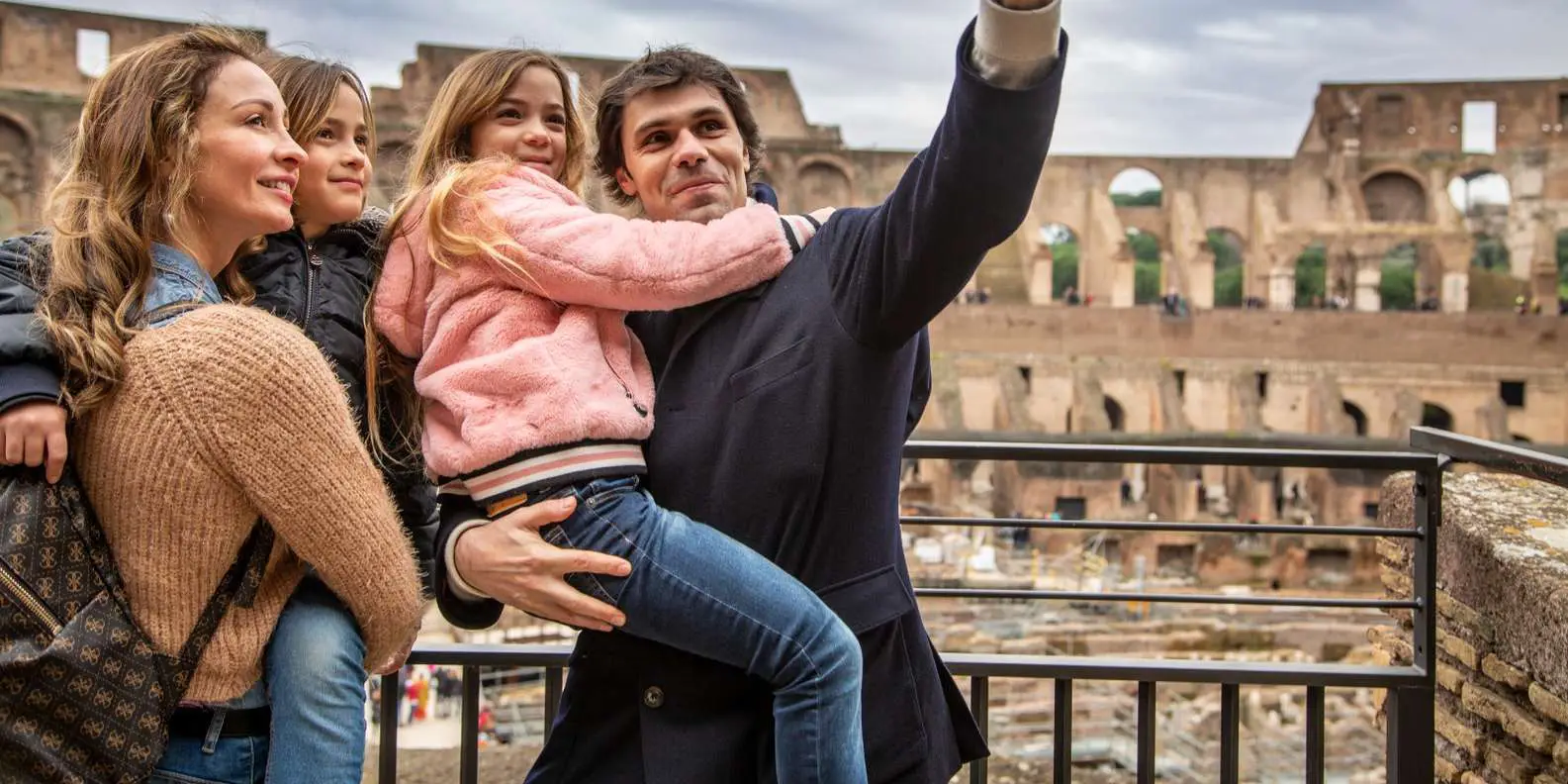 Família sorridente posando no Coliseu em Roma durante uma viagem em família para a Itália, em um dia ensolarado.