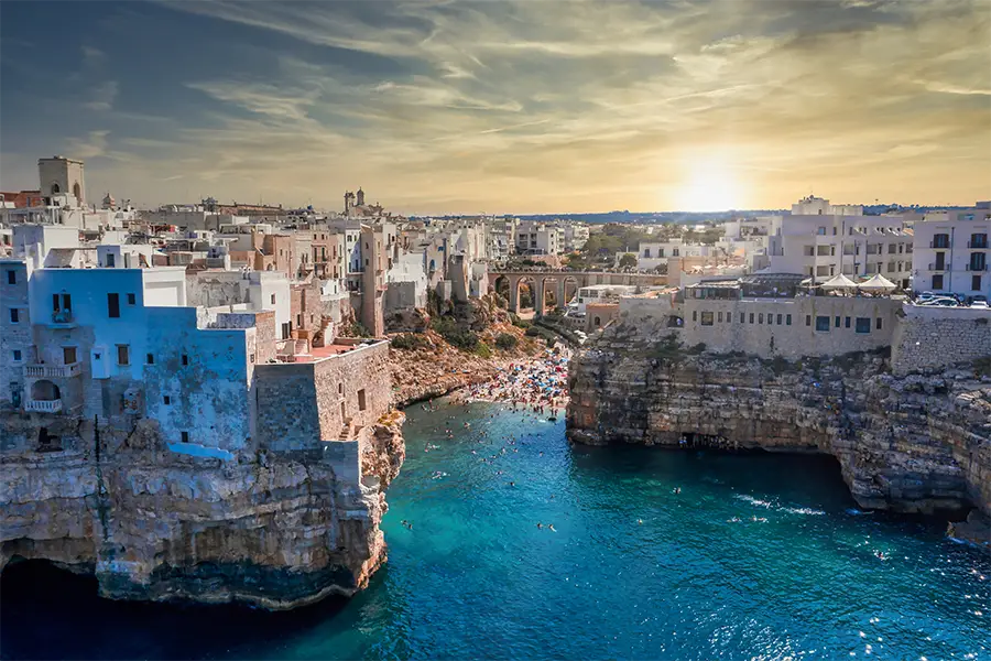 Vista aérea de Polignano a Mare com falésias, mar azul e praia escondida — ideal para passeios de barco na Itália explorando grutas e enseadas secretas.
