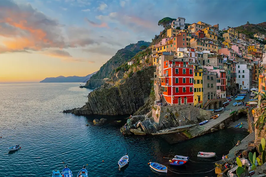 Barcos ancorados junto às casas coloridas de Riomaggiore ao pôr do sol, um clássico cenário para passeios de barco na Itália pela região de Cinque Terre.
