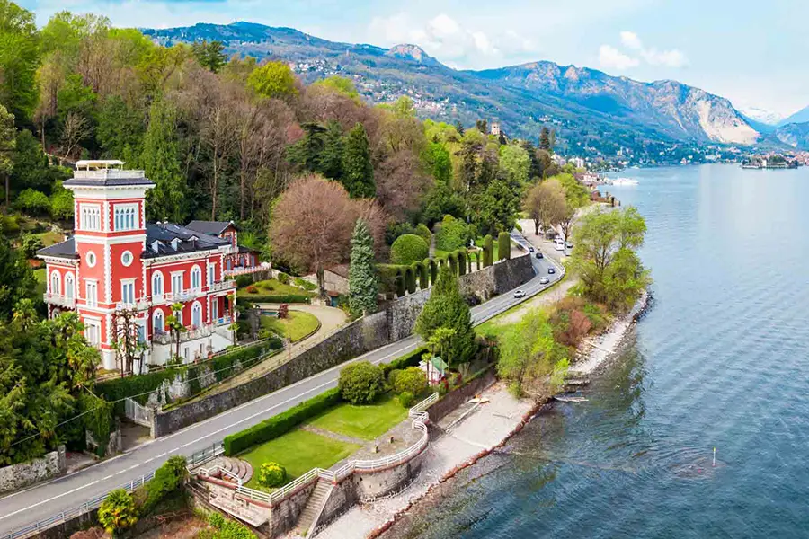 Elegante vila vermelha às margens do Lago Maggiore com estrada cênica à beira do lago e montanhas ao fundo