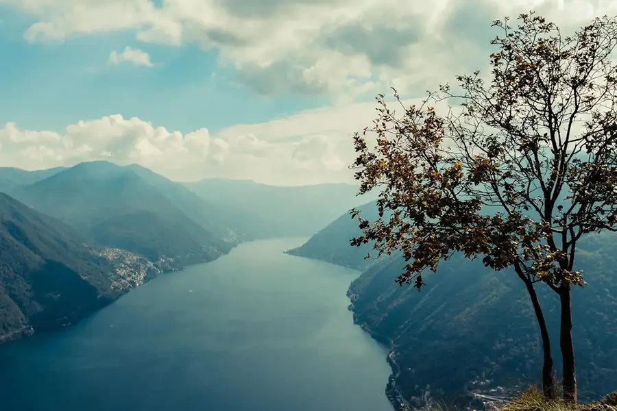 Vista panorâmica do Lago de Como a partir de Pigra, com montanhas ao fundo e árvore em primeiro plano