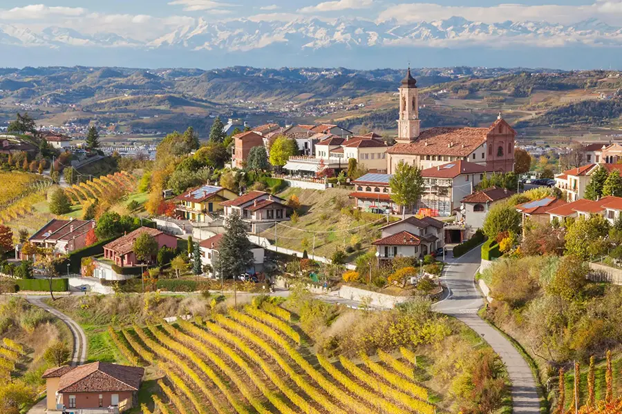 Vila no topo de uma colina no Piemonte cercada por vinhedos, com uma torre de igreja e os Alpes ao fundo