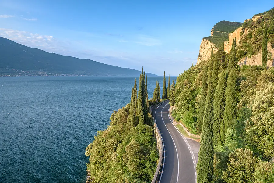 Estrada cênica Via Gardesana Occidentale ao longo do Lago de Garda com falésias, ciprestes e montanhas ao fundo