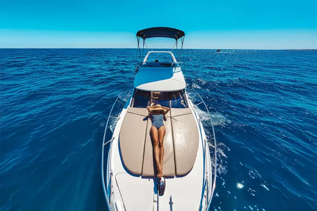 Mulher relaxando na parte frontal de um iate em mar azul cristalino sob céu aberto, durante um passeio de barco em estilo mediterrâneo.