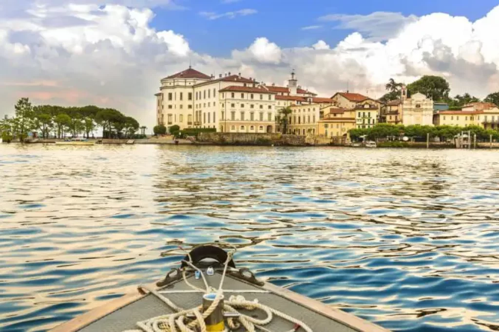 Vista da Ilha Bella no Lago Maggiore, Piemonte, Itália, com palácio histórico e construções à beira d’água, capturada a partir de um barco sobre as águas calmas do lago.